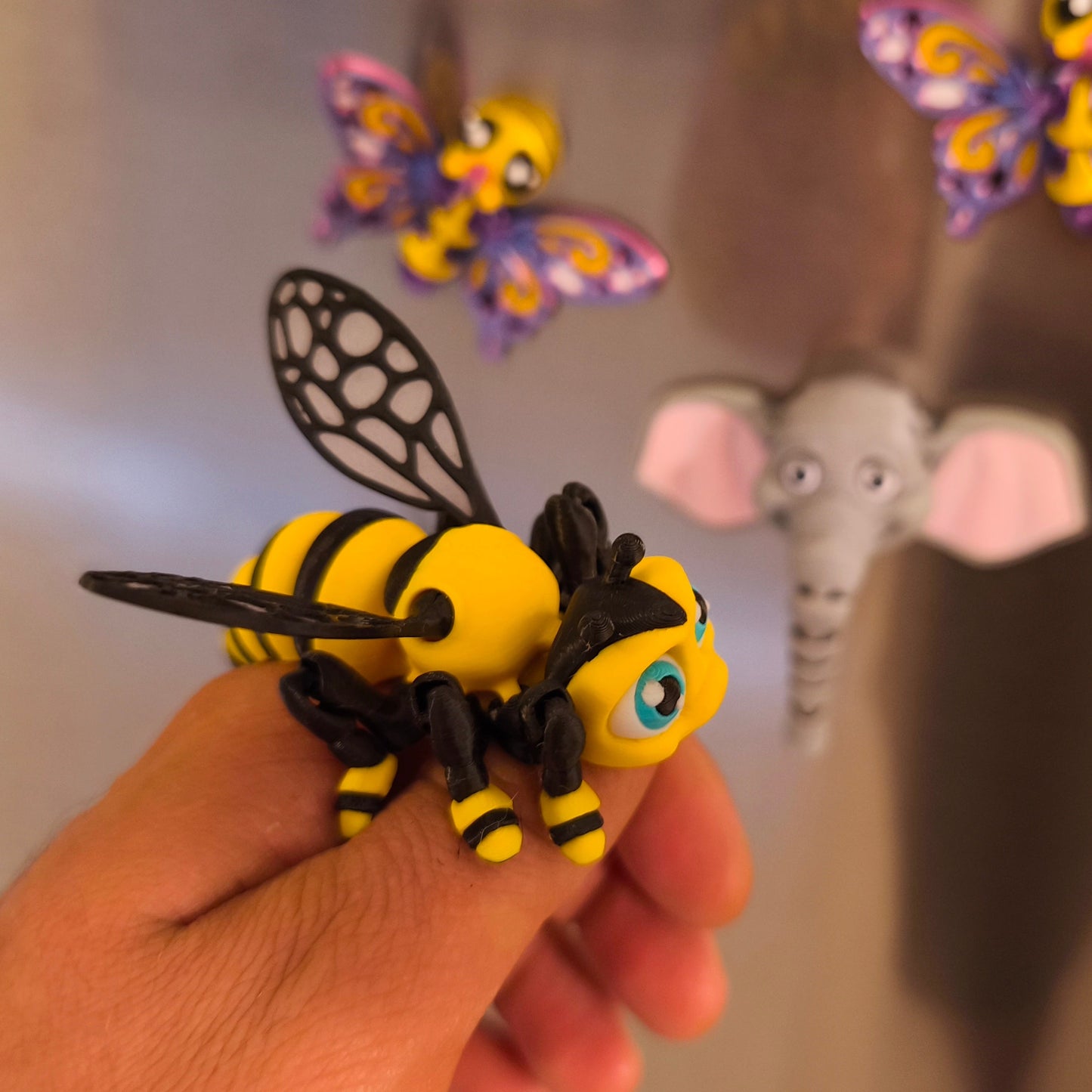 3D-gedruckter Bienen-Magnet Summi in der Hand, Seitenansicht, weitere Kühlschrankmagnete im Hintergrund, von 3DruckAS