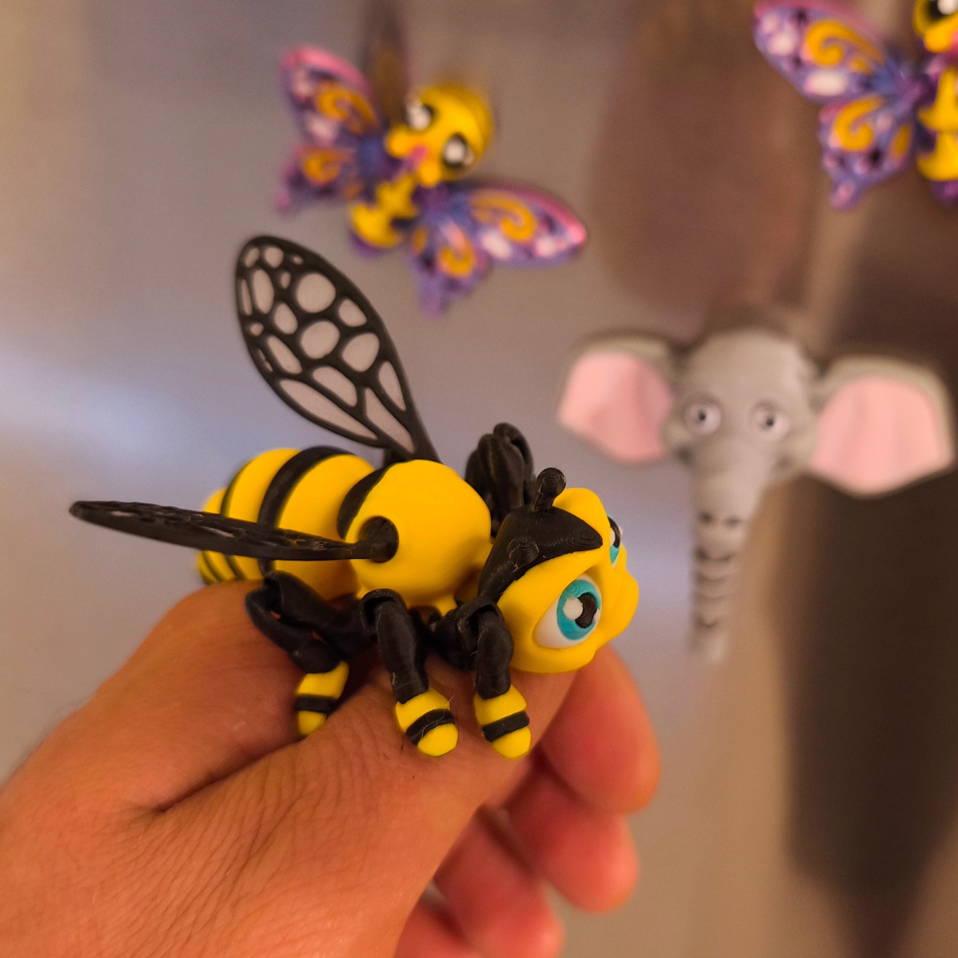 3D-gedruckter Bienen-Magnet Summi in der Hand, Seitenansicht, weitere Kühlschrankmagnete im Hintergrund, von 3DruckAS