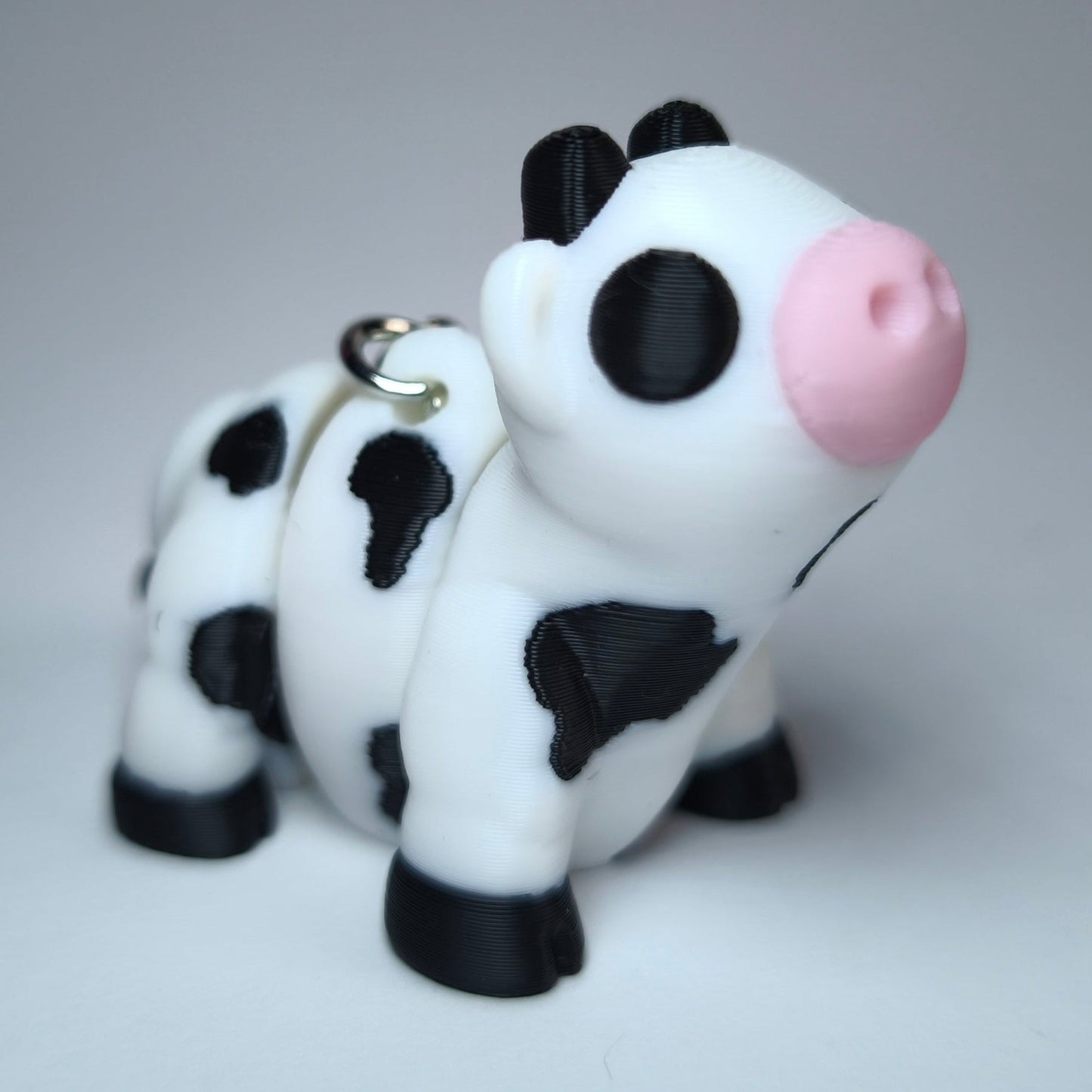 Linda die Flexi-Kuh – beweglicher 3D-gedruckter Schlüsselanhänger in Schwarz-Weiß mit rosa Schnauze.