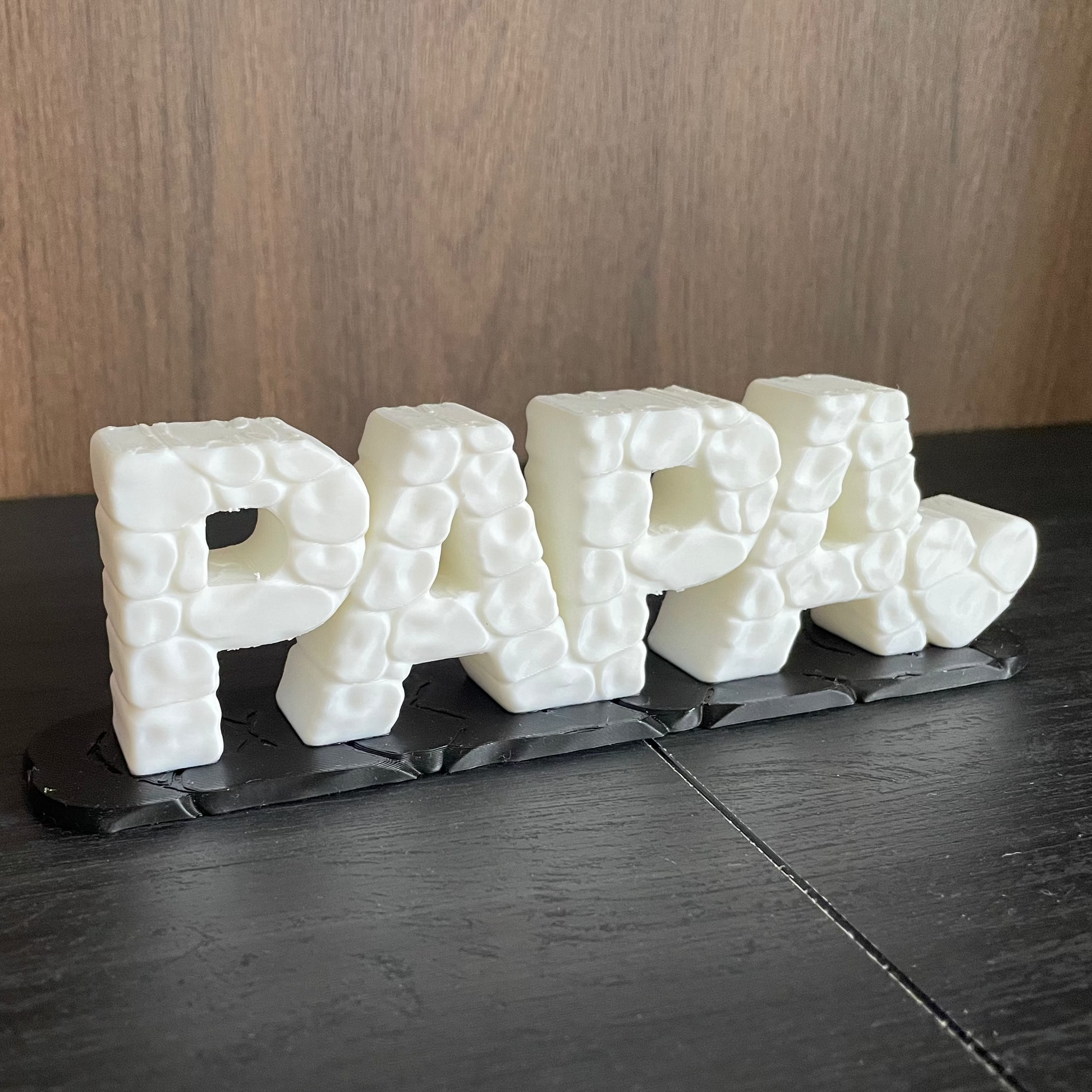 3D-gedruckter Schriftzug „PAPA" in Weiß mit Stein-Optik-Textur, Seitenansicht auf dunklem Untergrund, Tischdeko oder Geschenk für Papa, von 3DruckAS